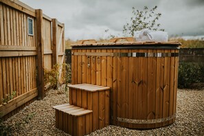 A wooden hot tub with steps, surrounded by a wooden fence and gravel.