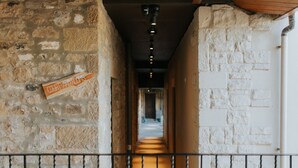 Ein Korridor mit Steinwänden, einem Holzschild mit der Aufschrift 'Courtyard Rooms' und einem Metallgeländer.