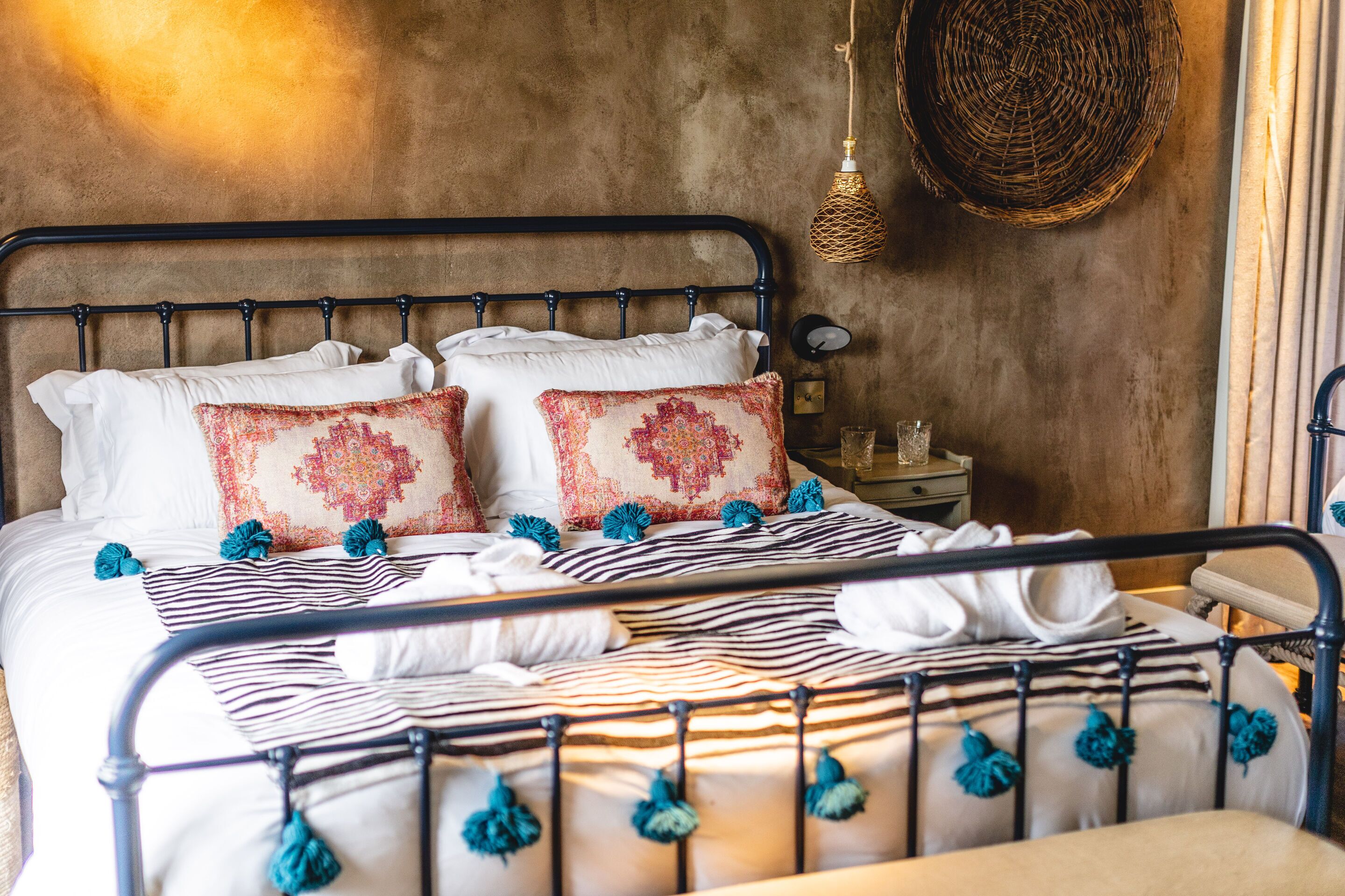 A bed with a metal frame, white and patterned pillows, and blue tassels.