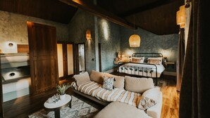 Ein gemütliches Schlafzimmer mit einem großen Bett, einem Schlafsofa und einem kleinen Tisch. Holzdecke und ein großes Fenster sind vorhanden.
