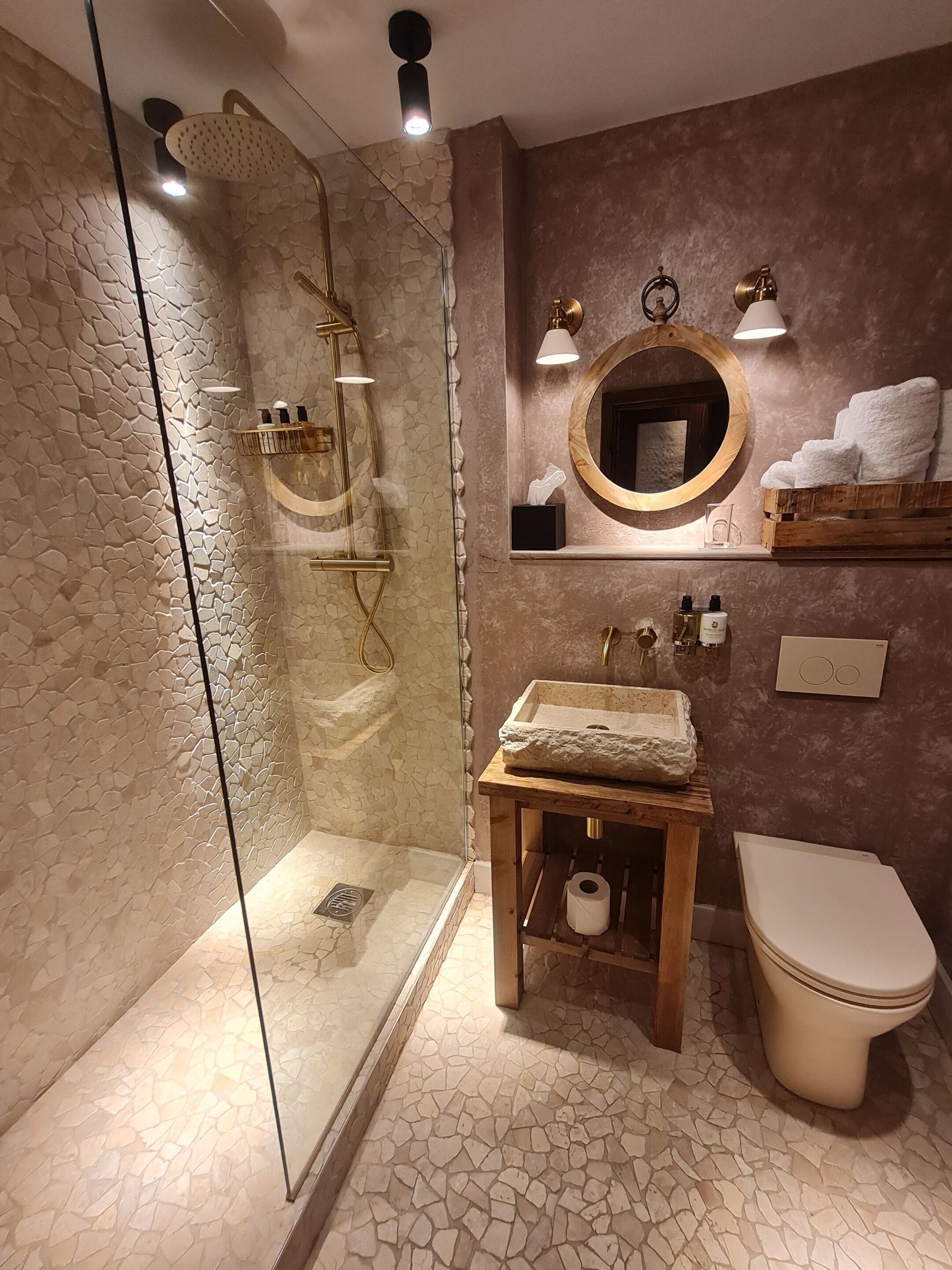 A bathroom with a glass-enclosed shower, a wooden vanity, a toilet, and a mirror with a wooden frame.