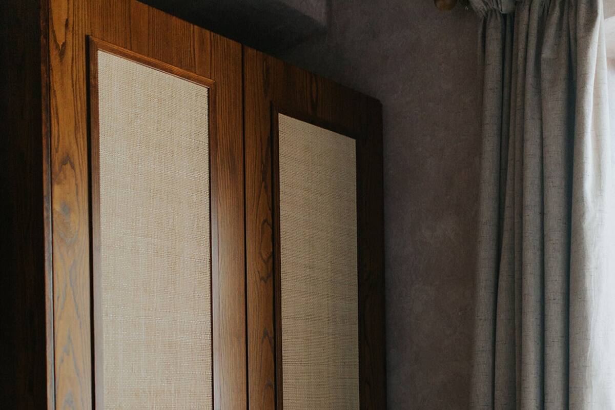 A room with a wooden wardrobe, a metal bed frame, and a window with curtains.