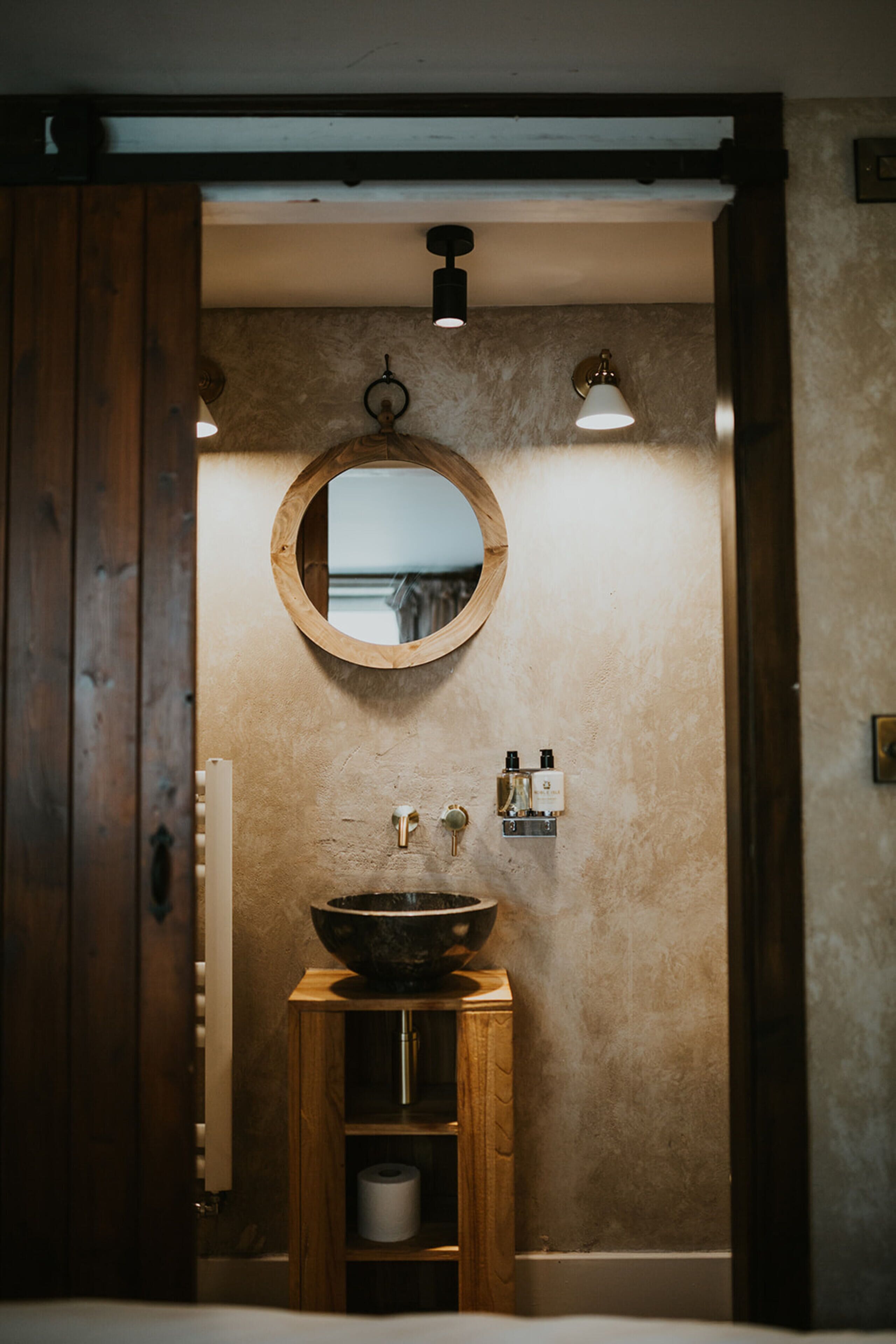 A bathroom with a wooden vanity, a round mirror, and a large sink.