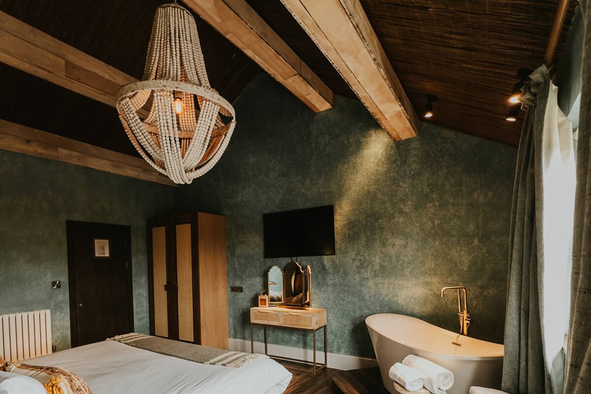 A bedroom with a large bed, a vanity with a bathtub, and a seating area with chairs.
