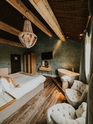 A bedroom with a large bed, a vanity with a bathtub, and a seating area with chairs.
