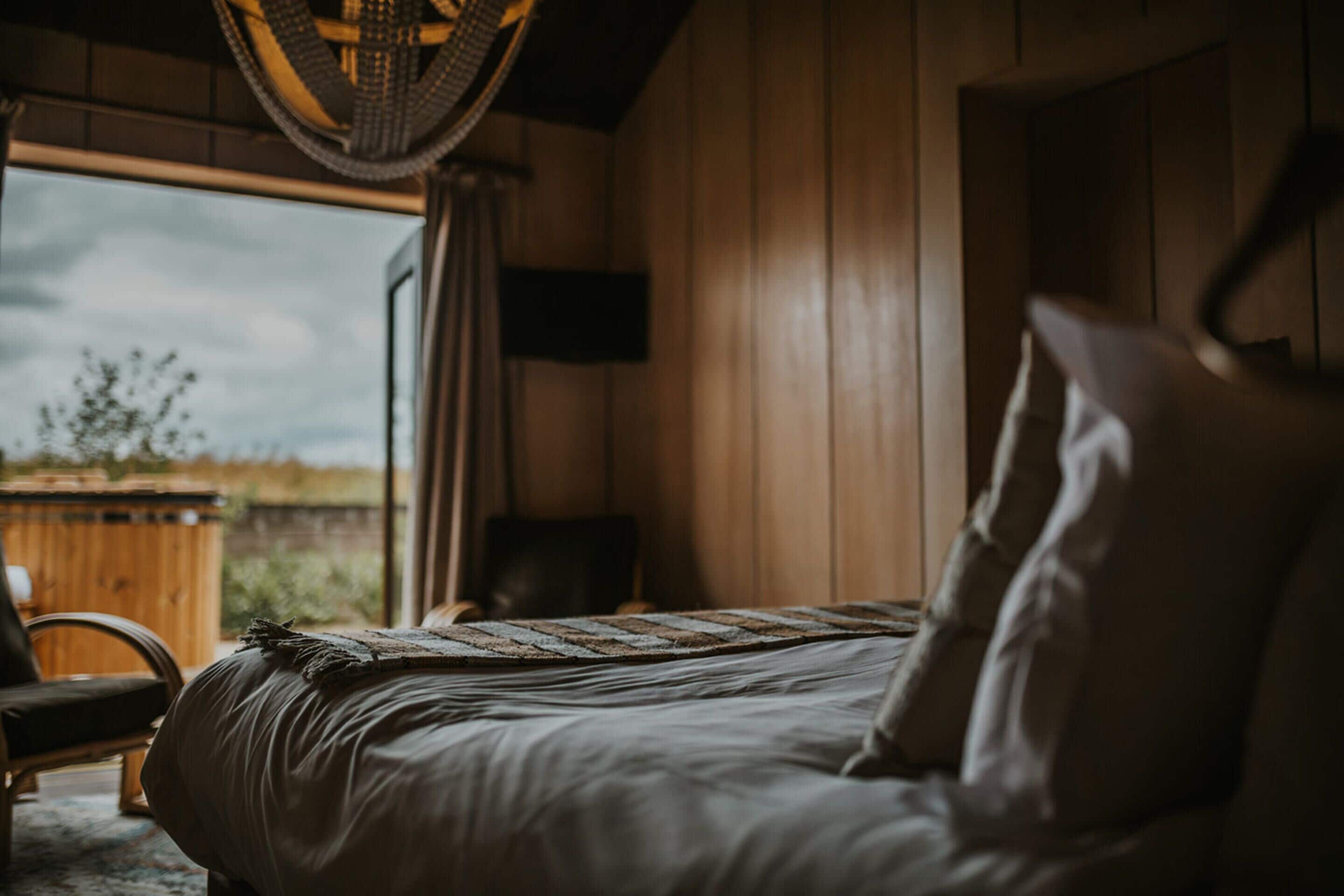 A bedroom with a bed, a chair, a window, and a wooden wall.