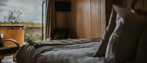 A bedroom with a bed, a chair, a window, and a wooden wall.