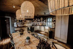 Una cocina rústica con armarios de madera, una mesa grande de madera y lámparas colgantes de mimbre.