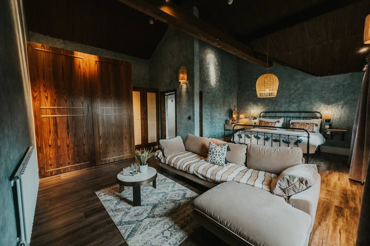 A cozy bedroom with a wooden ceiling, a bed with patterned bedding, a nightstand, and a hanging light fixture.