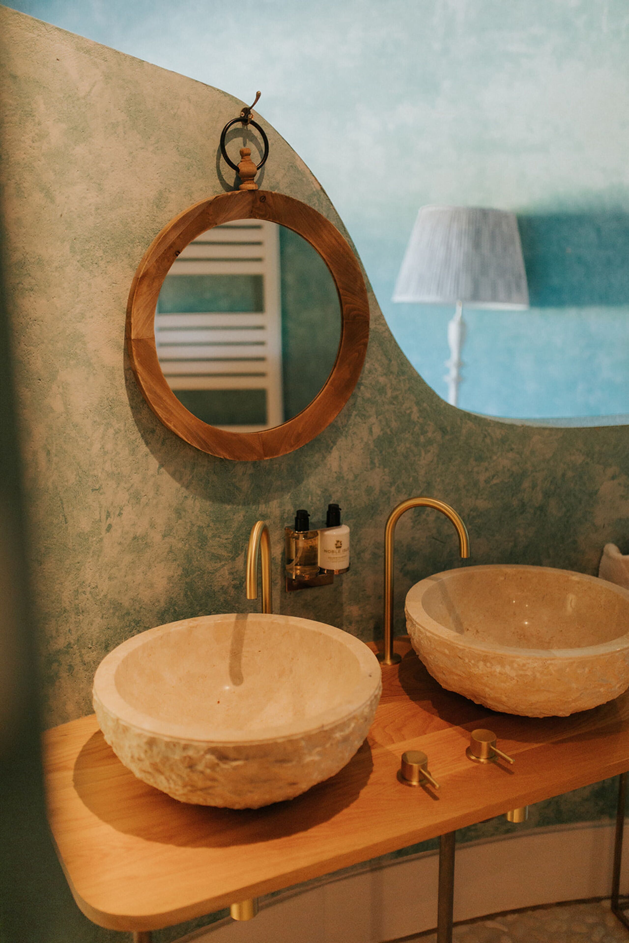 A bathroom with two large stone sinks, a wooden vanity, and a round mirror.
