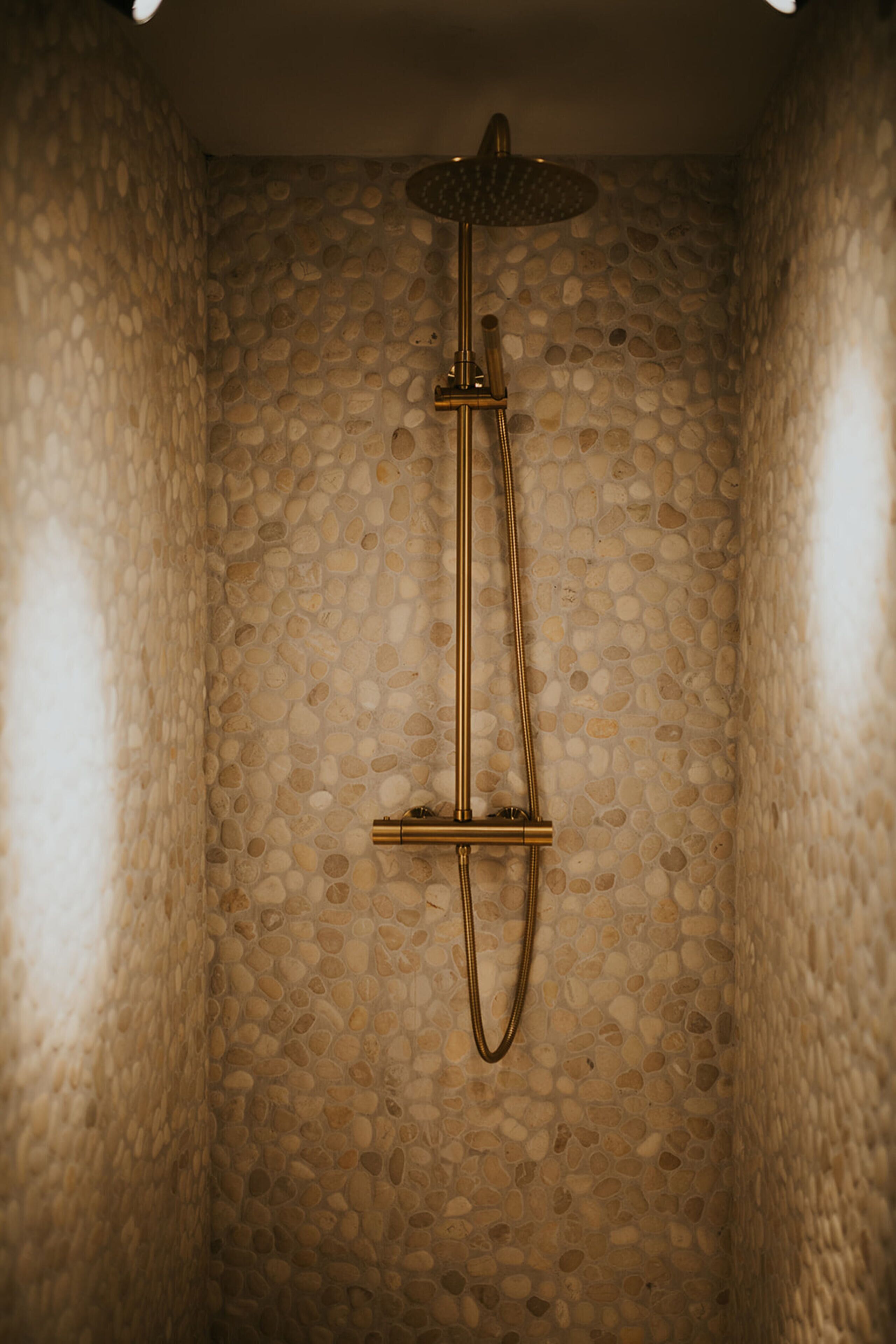 Eine Dusche mit Steinwand und goldfarbener Duschbrause.
