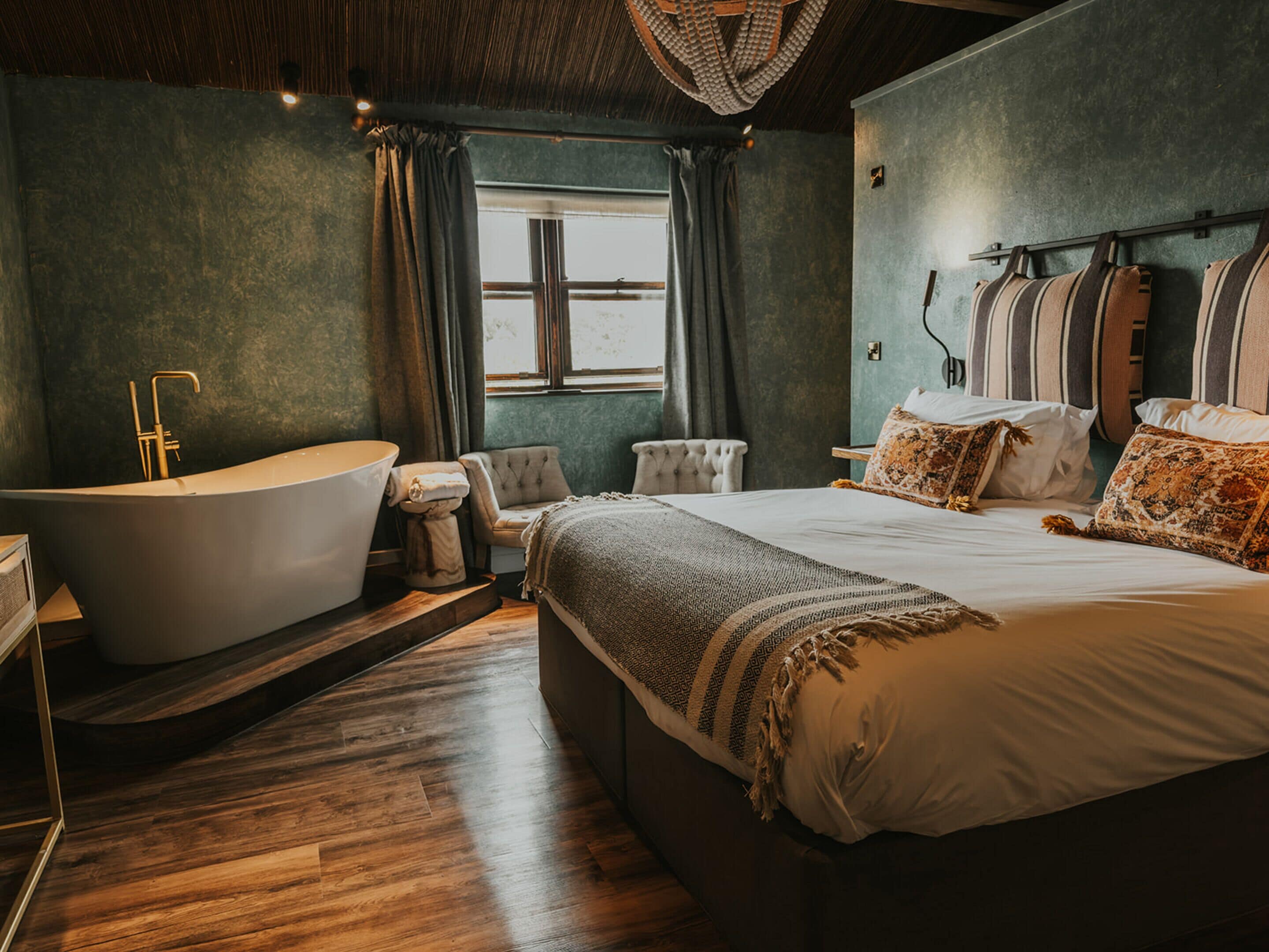 A modern bedroom with a large bed, a freestanding bathtub, and a window with curtains.
