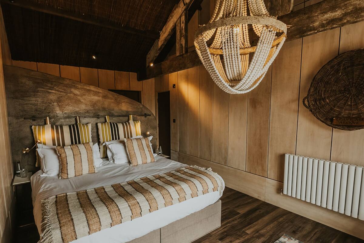 A bedroom with a large bed, wooden walls, a woven chandelier, and a patterned rug.