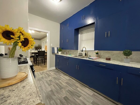 A modern kitchen with blue cabinets, a marble countertop, and a wooden floor.