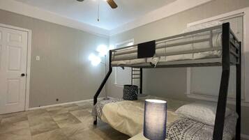 Une chambre avec un lit superposé, un ventilateur de plafond, une lampe et une porte.
