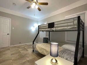 Une chambre avec un lit superposé, un ventilateur de plafond, une lampe et une porte.