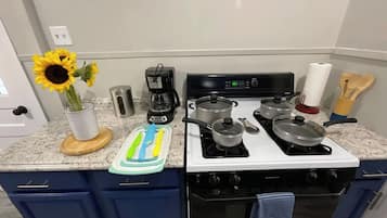Une cuisine équipée d’une cuisinière, de casseroles, d’une machine à café et d’un vase rempli de tournesols.