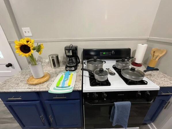 Une cuisine équipée d’une cuisinière, de casseroles, d’une machine à café et d’un vase rempli de tournesols.