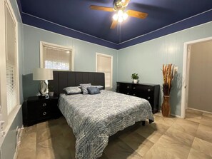 A bedroom with a bed, nightstands, a ceiling fan, and a window with blinds.