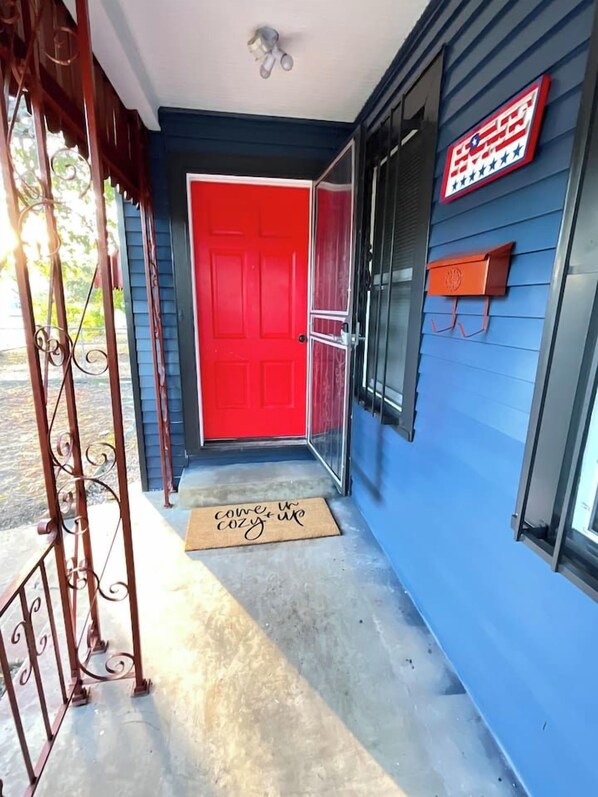 A red door with a doormat, a blue exterior wall, and a small orange mailbox.