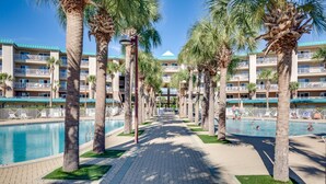 Un hotel con zona de piscina, palmeras y un cielo azul despejado.