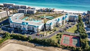 Vista aérea de un resort con varias construcciones, una playa y una cancha de tenis.