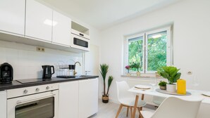 A modern kitchen with white cabinets, a built-in oven, and a dining area with a table and chairs. - EG L 70m2 2-Zimmer Wohnung (Freilassing)