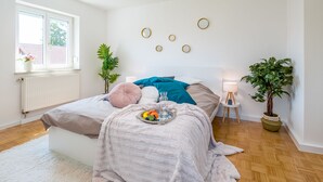 A bedroom with a bed, bedside table, lamp, potted plants, and a window. - EG L 70m2 2-Zimmer Wohnung (Freilassing)