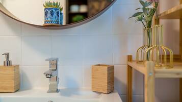 Un bagno con un lavandino bianco, un armadietto in legno, uno specchio e un vaso con fiori.