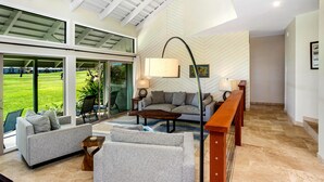 A spacious living area with a large window, a sofa, a coffee table, and a lamp.