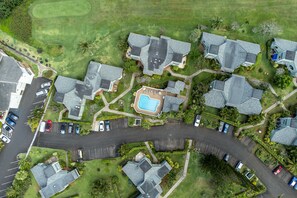 An aerial view of a residential area with multiple houses, a swimming pool, and a curved road.