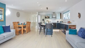 Eine moderne Küche mit Kochinsel, Essbereich mit Stühlen und ein Wohnzimmer mit Sofa und Couchtisch.