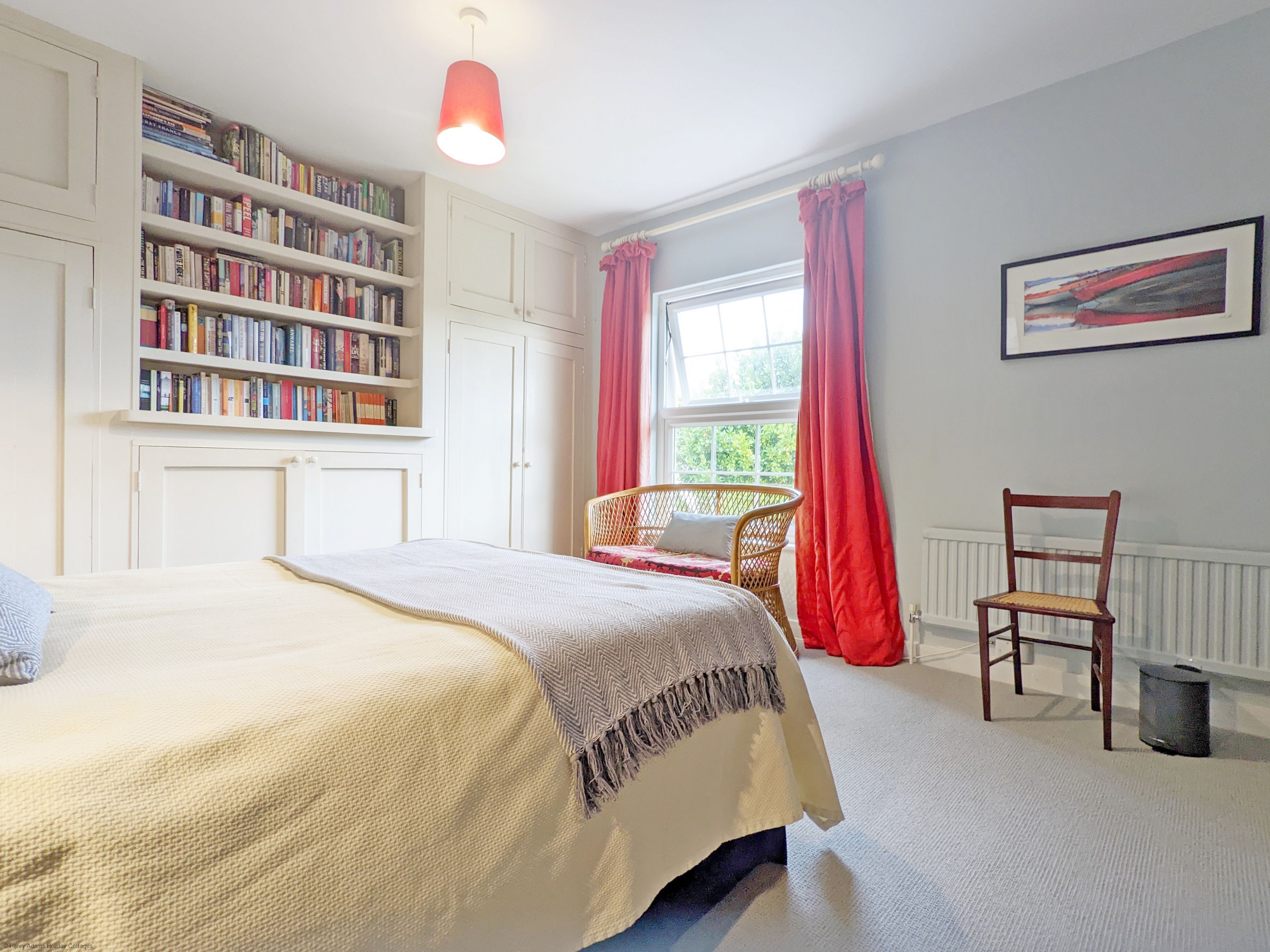 A bedroom with a bed, a bookshelf, a window with curtains, a chair, and a radiator.