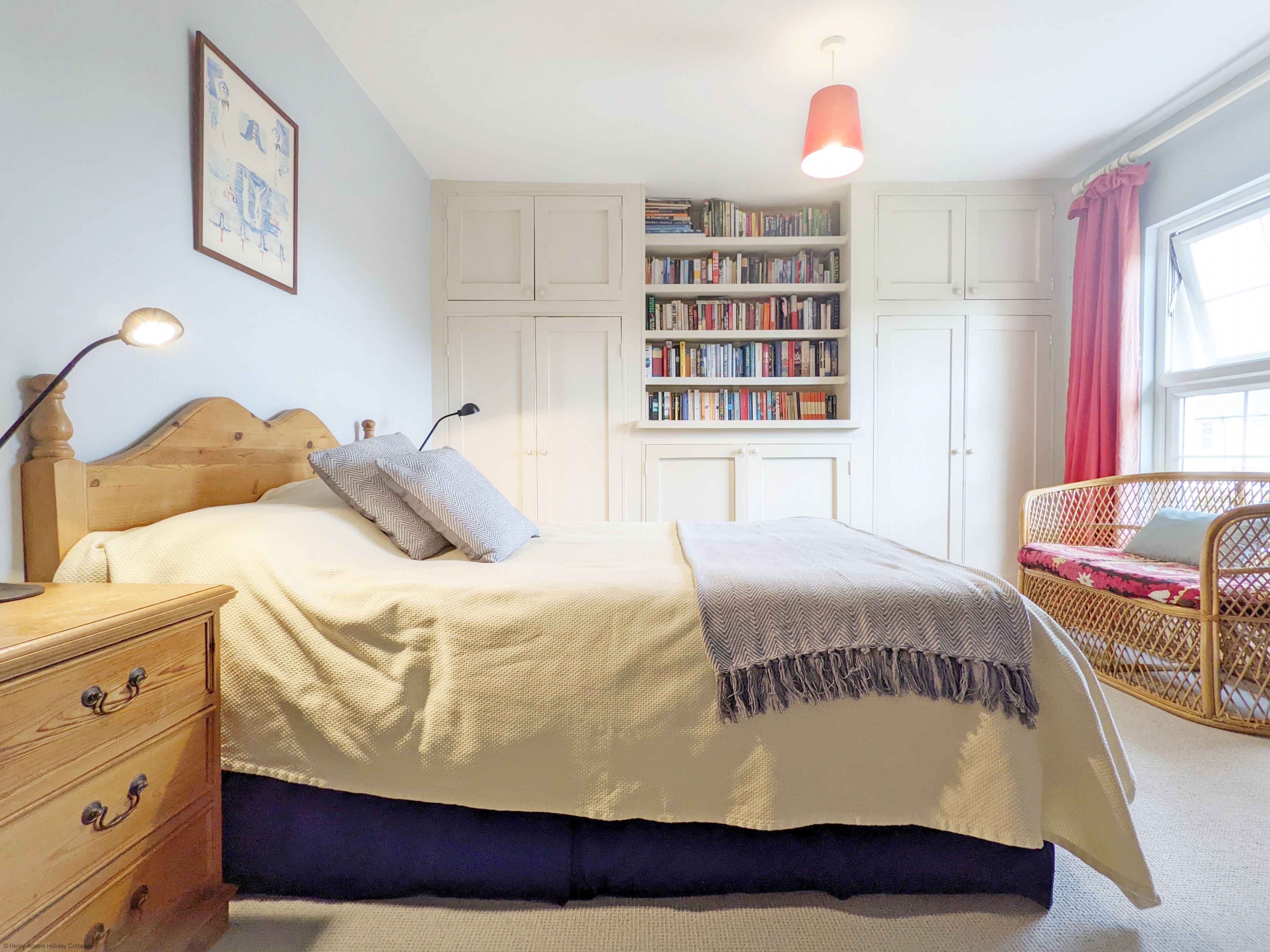 Ein Schlafzimmer mit einem Bett, Nachttischen, einem Bücherregal und einem Fenster mit Vorhängen.