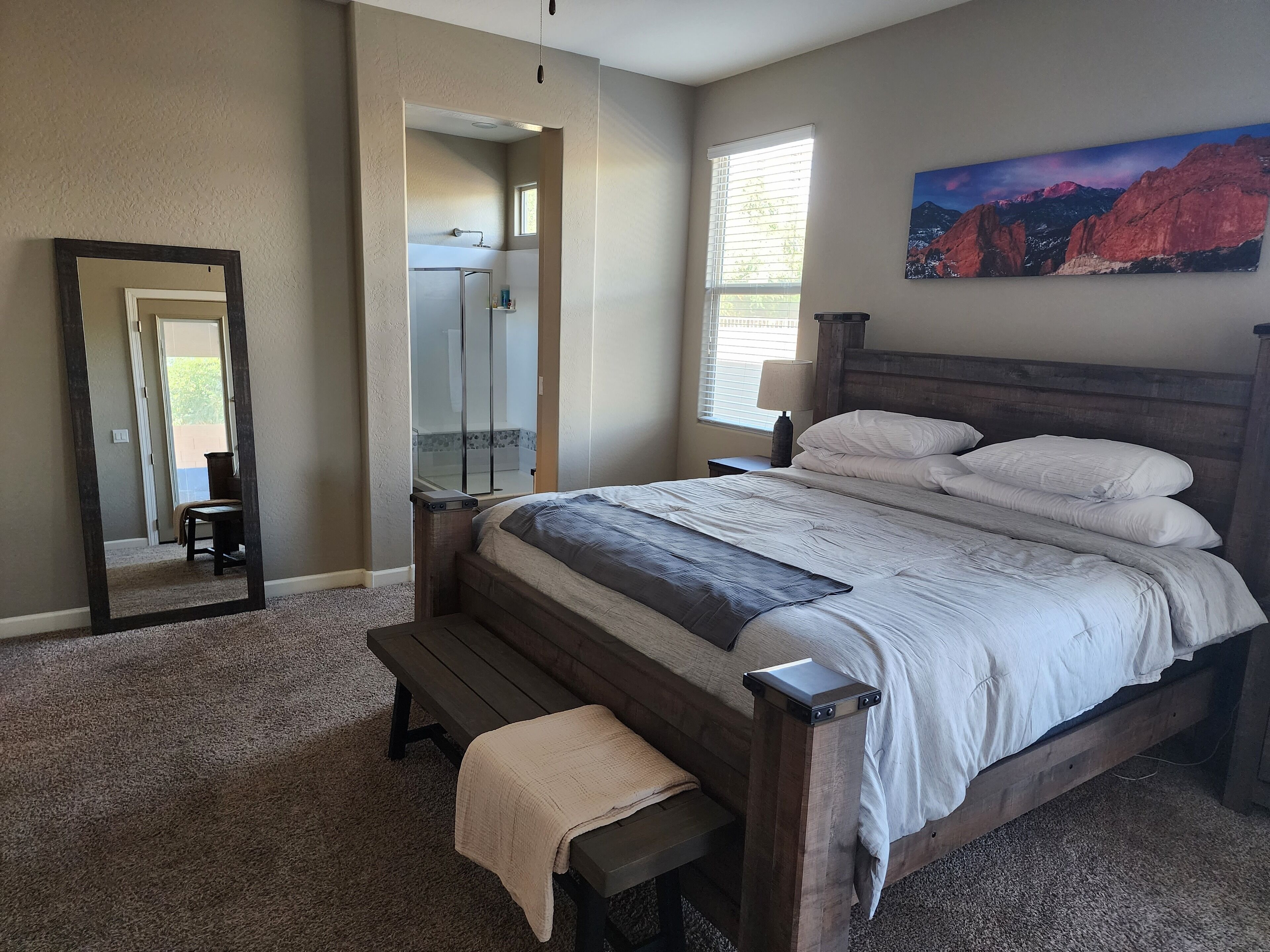A bedroom with a large bed, a wooden bench, a mirror, and a painting on the wall.