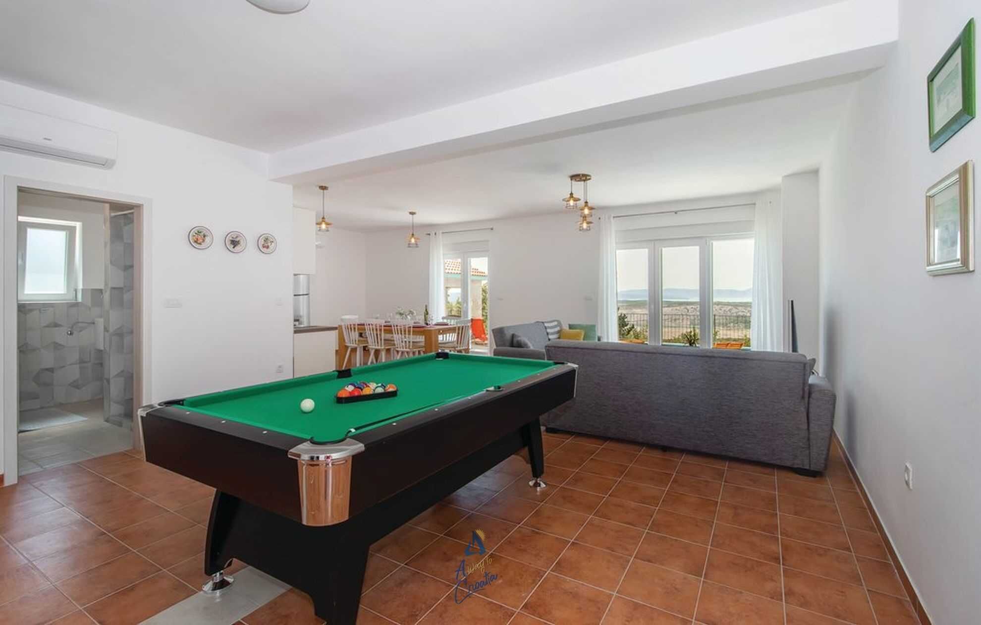 A pool table in a room with a dining area and a view of the outdoors.