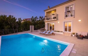 Una casa de dos pisos con piscina, mobiliario exterior y balcón.