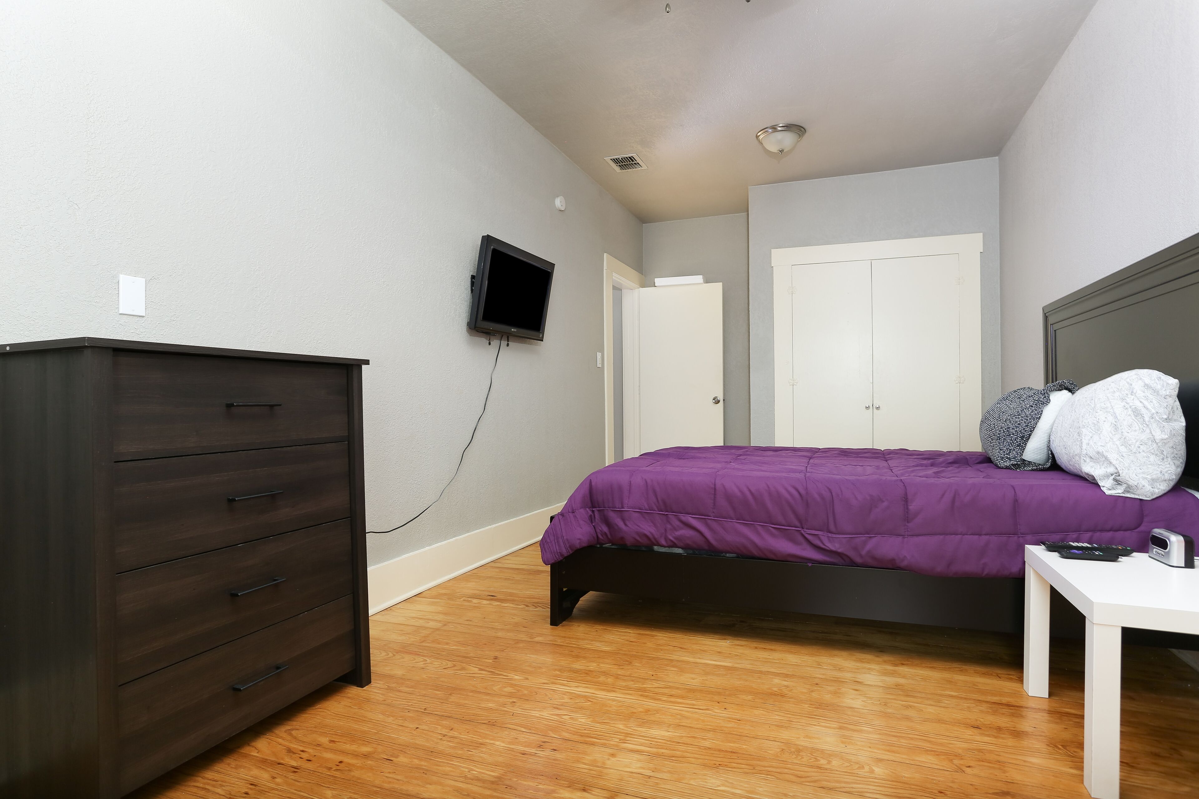 Une chambre à coucher avec un lit, une commode, un téléviseur et une porte.