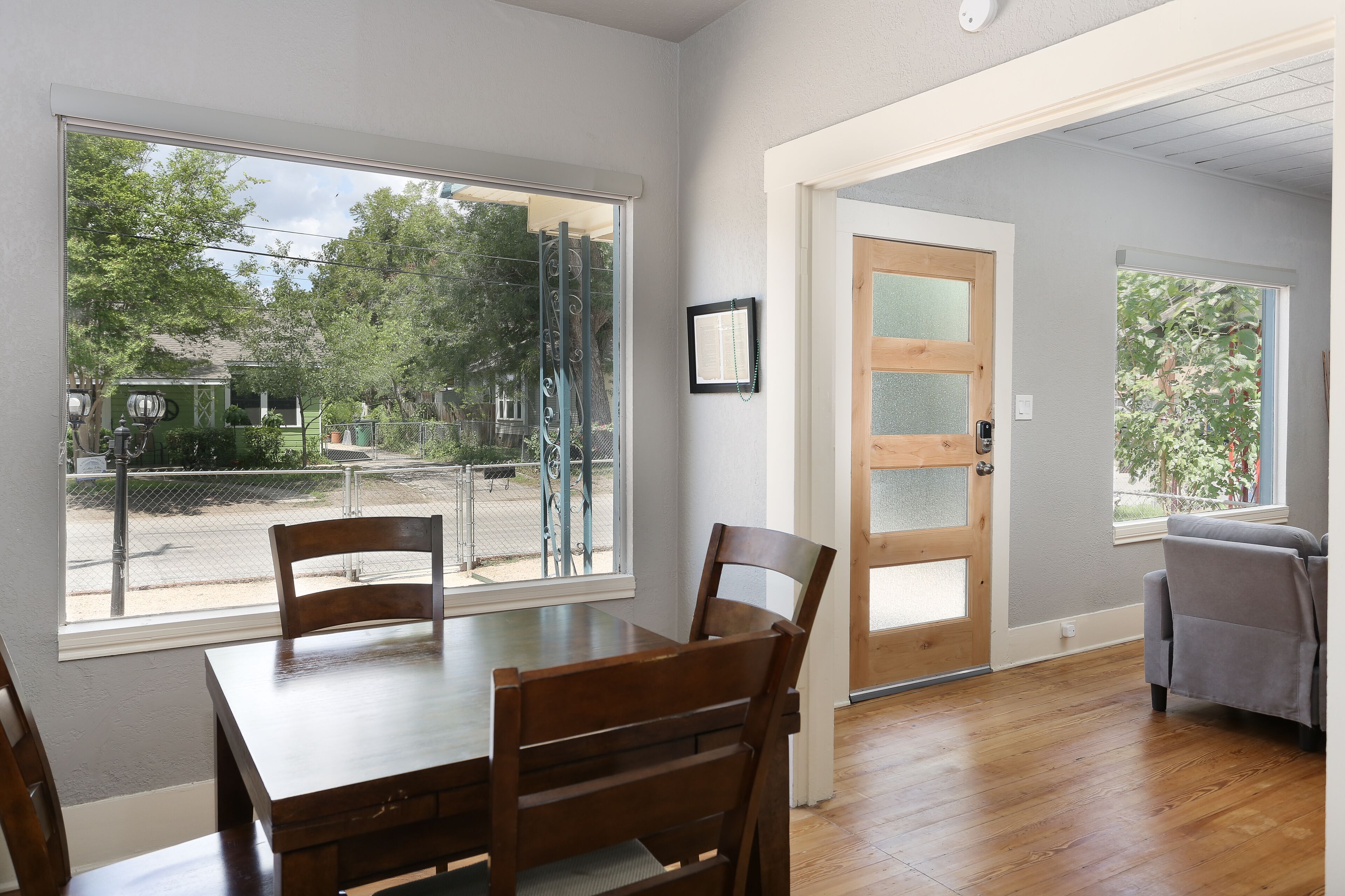 Un comedor con una mesa y sillas de madera, un ventanal con vistas a un patio de juegos y una puerta que da a otra habitación.