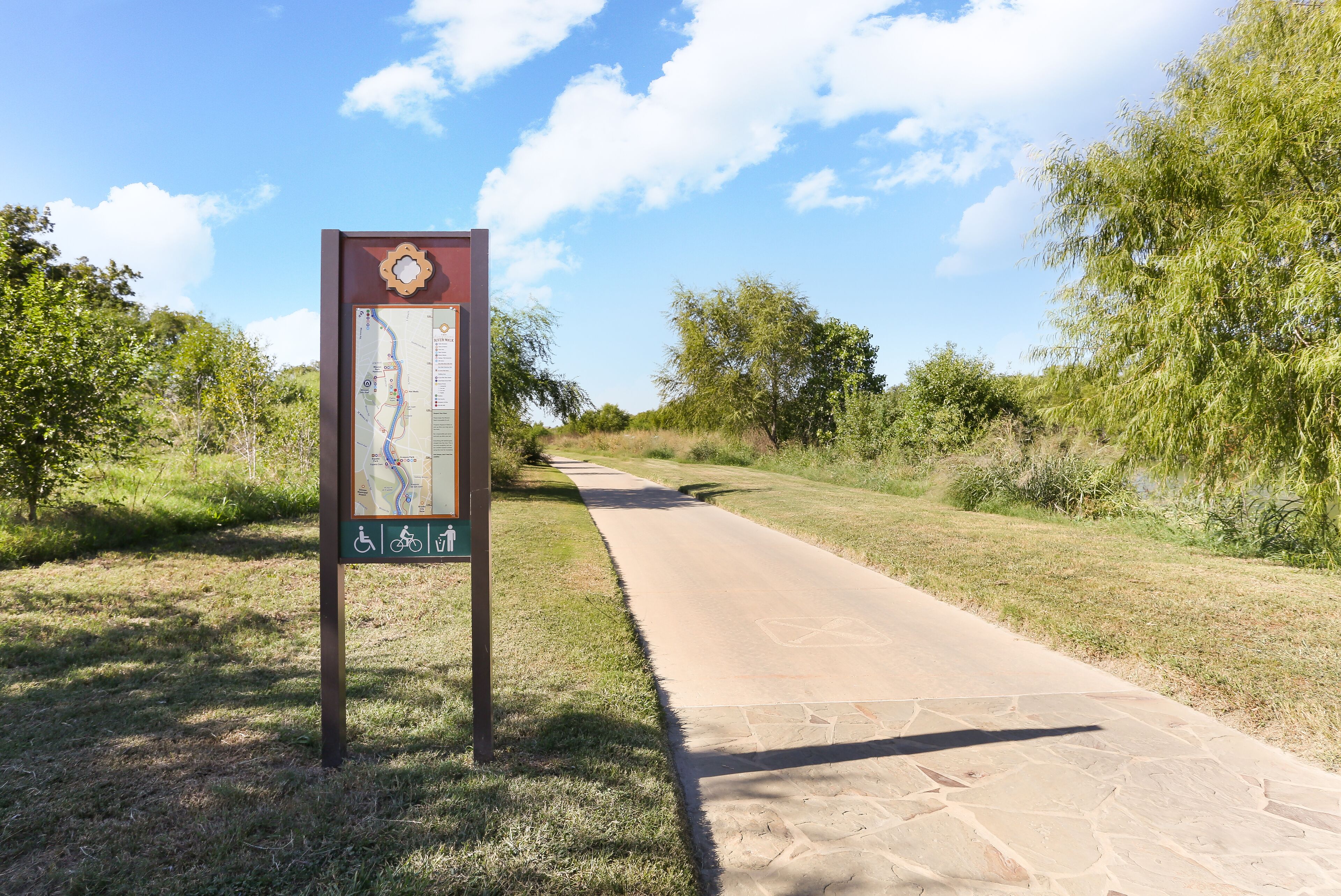 A paved pathway with a map sign on the left, surrounded by greenery.