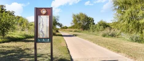 A paved pathway with a map sign on the left, surrounded by greenery.