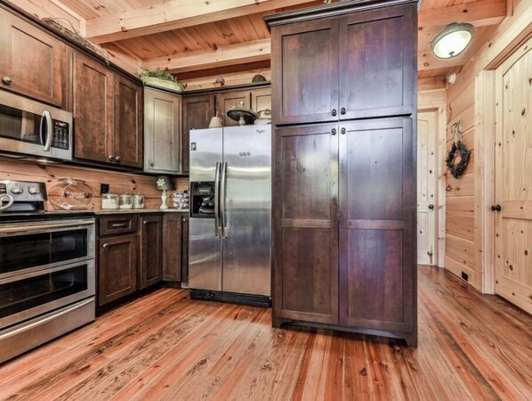A kitchen with wooden cabinets, stainless steel appliances, and a wooden floor.