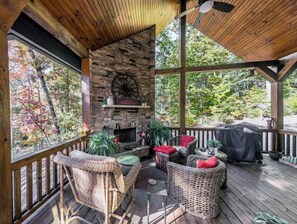 Relax by the stone fireplace, surrounded by wicker furniture and a grill, with views of the surrounding trees.