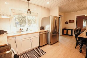 Une cuisine moderne avec des meubles blancs, des appareils en acier inoxydable et un coin repas comprenant une table et des chaises en bois.