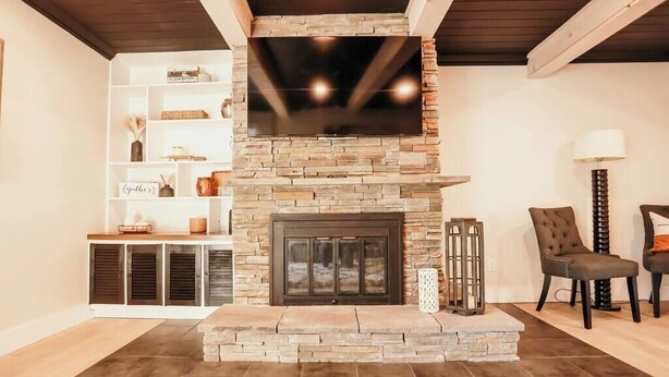 A living room with a stone fireplace, a flat-screen TV mounted above it, a bookshelf, and two chairs. - Spacious 4 bedroom Guest House (Clare)