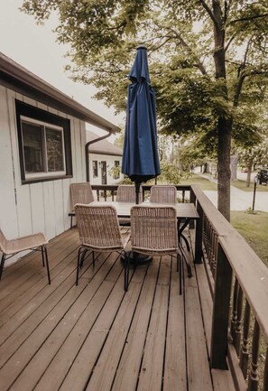 A wooden deck with wicker chairs and a table, a blue umbrella, and a house in the background. - Spacious 4 bedroom Guest House with Hot Tub (Clare)