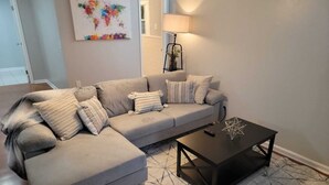 Una sala de estar con un sofá modular gris, una mesa de centro negra y una alfombra estampada.
