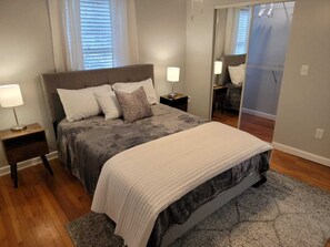 A bedroom with a large bed, two bedside tables, a mirror, and a window with blinds. - Downtown Fully Furnished Renovated Bungalow Allowing Pets (Savannah)