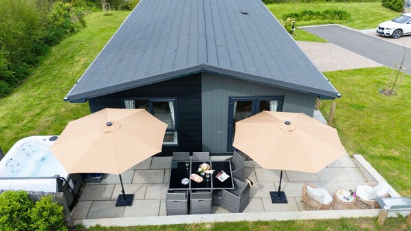 A house with a patio area featuring two outdoor umbrellas, a hot tub, and wicker furniture.