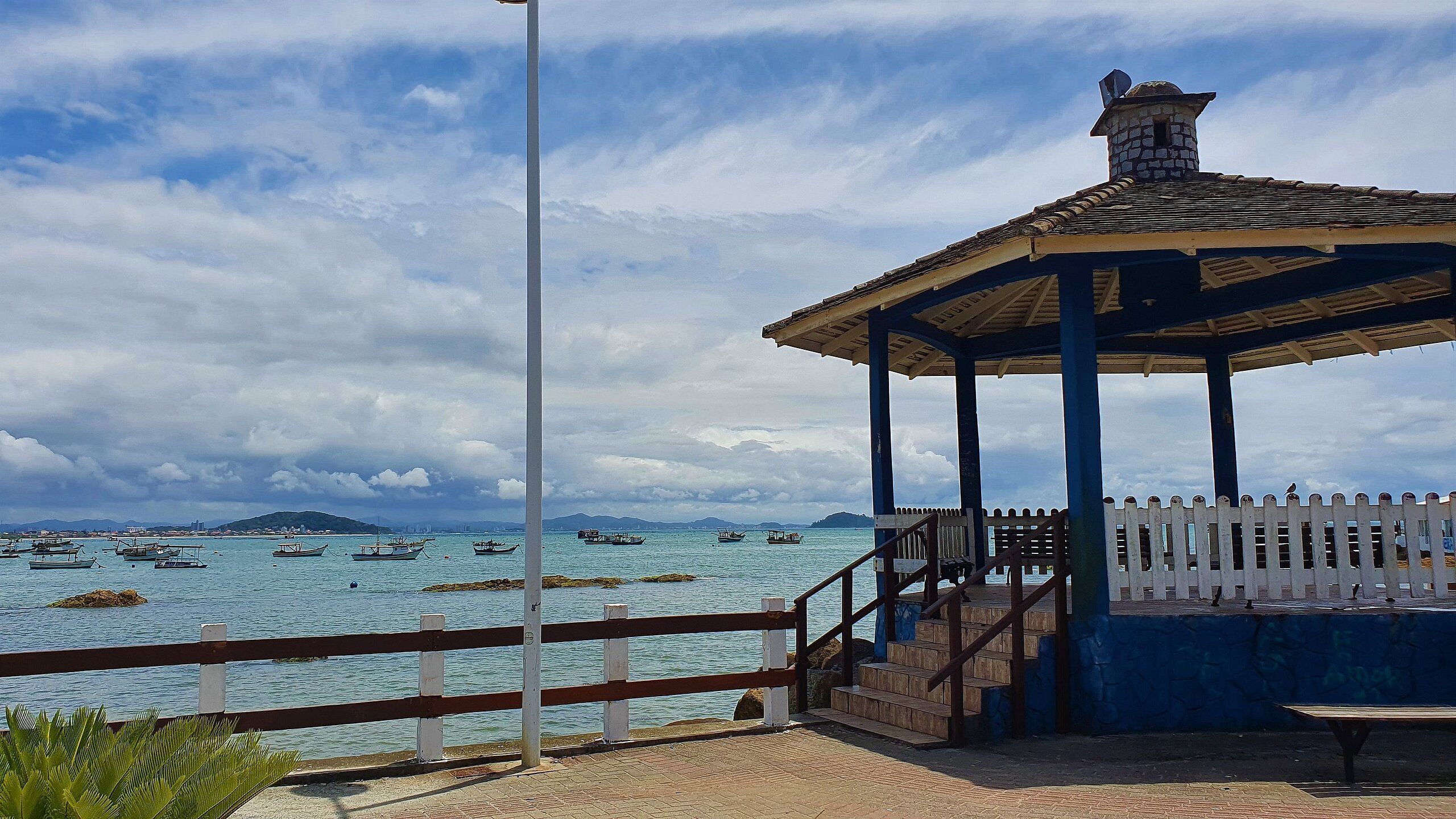 A gazebo with a tiled roof overlooking a body of water with boats.